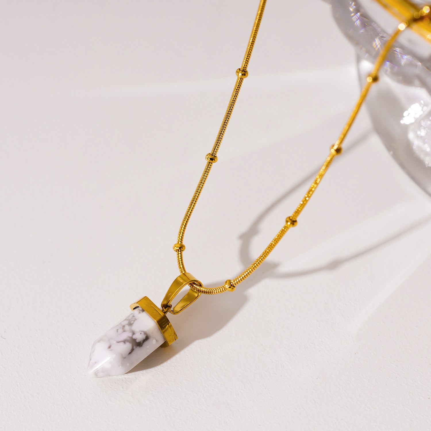 AMELIE : Collier avec pendentif en pierre turquoise blanche, accroché à une chaîne perlée texturée imitant la peau de serpent.