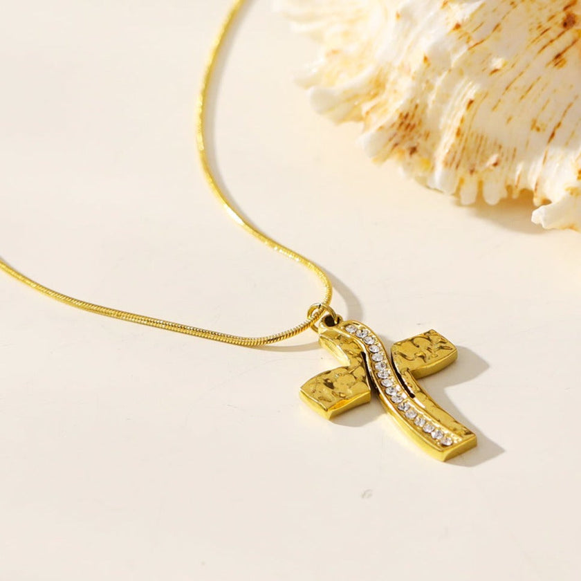 ARCASSA : Pendentif croix en zircone incrusté avec finition martelée, porté sur un mini collier à chaîne texturée imitation peau de serpent.