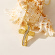ARCASSA : Pendentif croix en zircone incrusté avec finition martelée, porté sur un mini collier à chaîne texturée imitation peau de serpent.