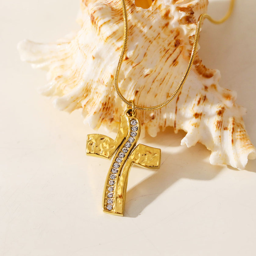ARCASSA : Pendentif croix en zircone incrusté avec finition martelée, porté sur un mini collier à chaîne texturée imitation peau de serpent.