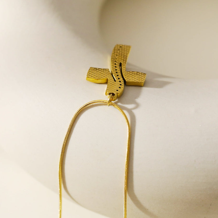 ARCASSA : Pendentif croix en zircone incrusté avec finition martelée, porté sur un mini collier à chaîne texturée imitation peau de serpent.