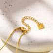 ARCASSA : Pendentif croix en zircone incrusté avec finition martelée, porté sur un mini collier à chaîne texturée imitation peau de serpent.