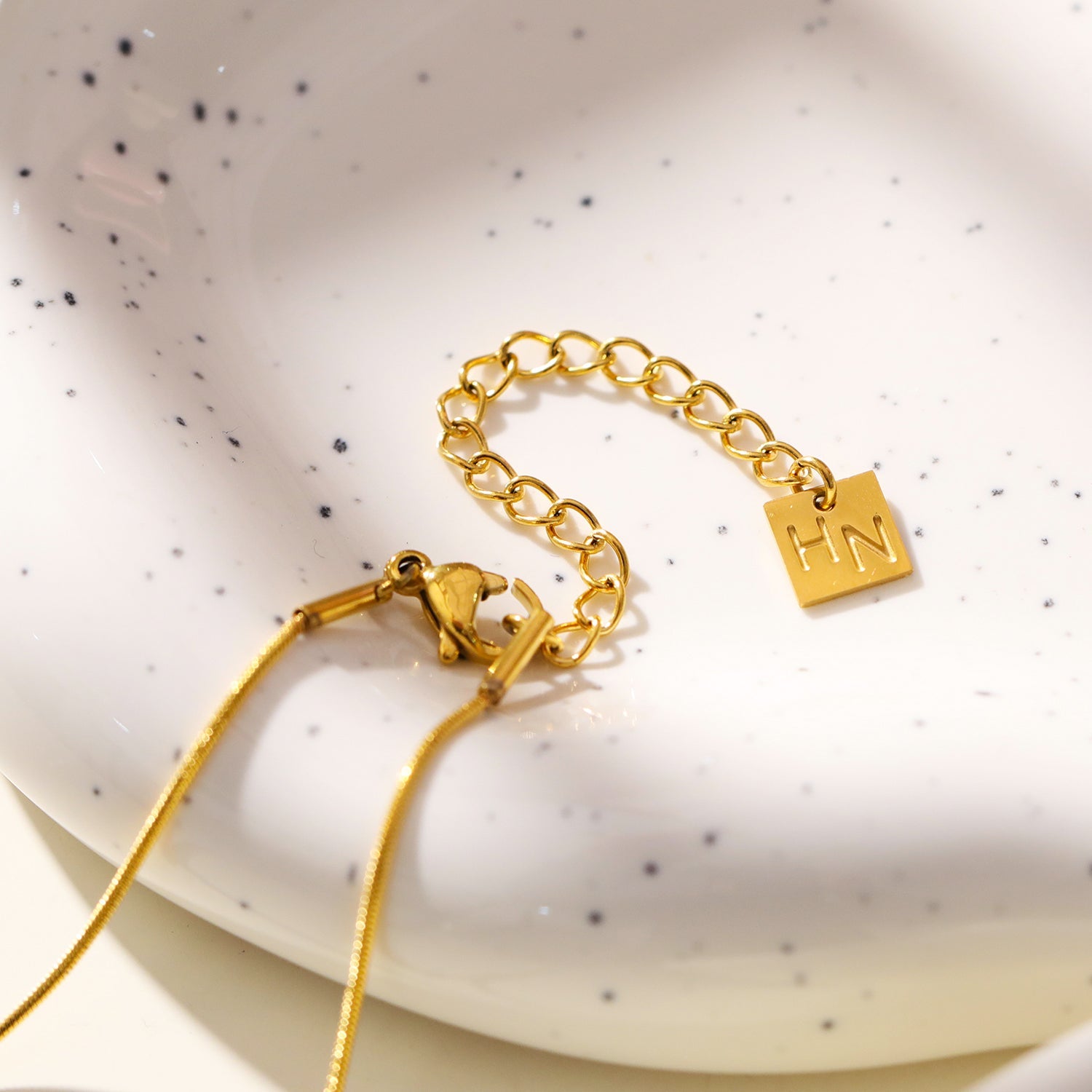 ARCASSA : Pendentif croix en zircone incrusté avec finition martelée, porté sur un mini collier à chaîne texturée imitation peau de serpent.