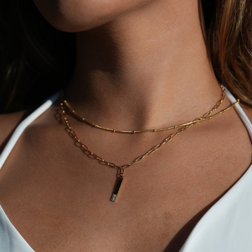 Style KORATIA : Collier minimaliste avec chaîne à maillons plats et pendentif barre en or incrusté de zircone.