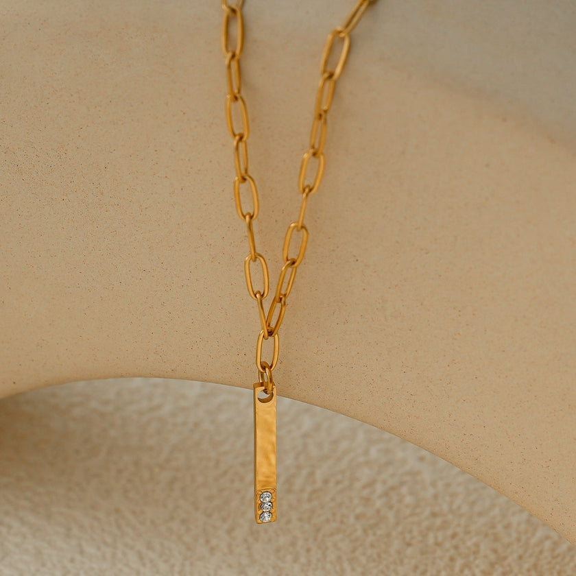 Style KORATIA : Collier minimaliste avec chaîne à maillons plats et pendentif barre en or incrusté de zircone.