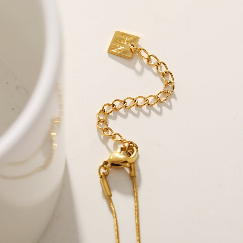Style DEFNIE : Collier délicat à chaîne texturée effet peau de serpent, agrémenté d'un trio de breloques.