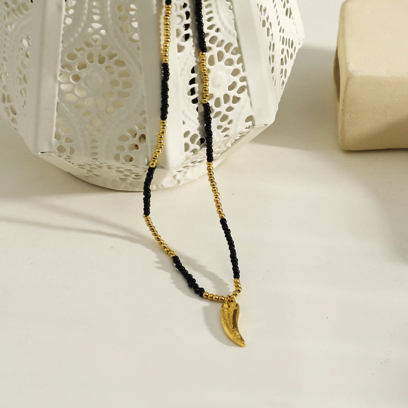 Collier RITA à chaîne perlée noir et or avec pendentif dent en or gravé.