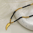 Collier RITA à chaîne perlée noir et or avec pendentif dent en or gravé.