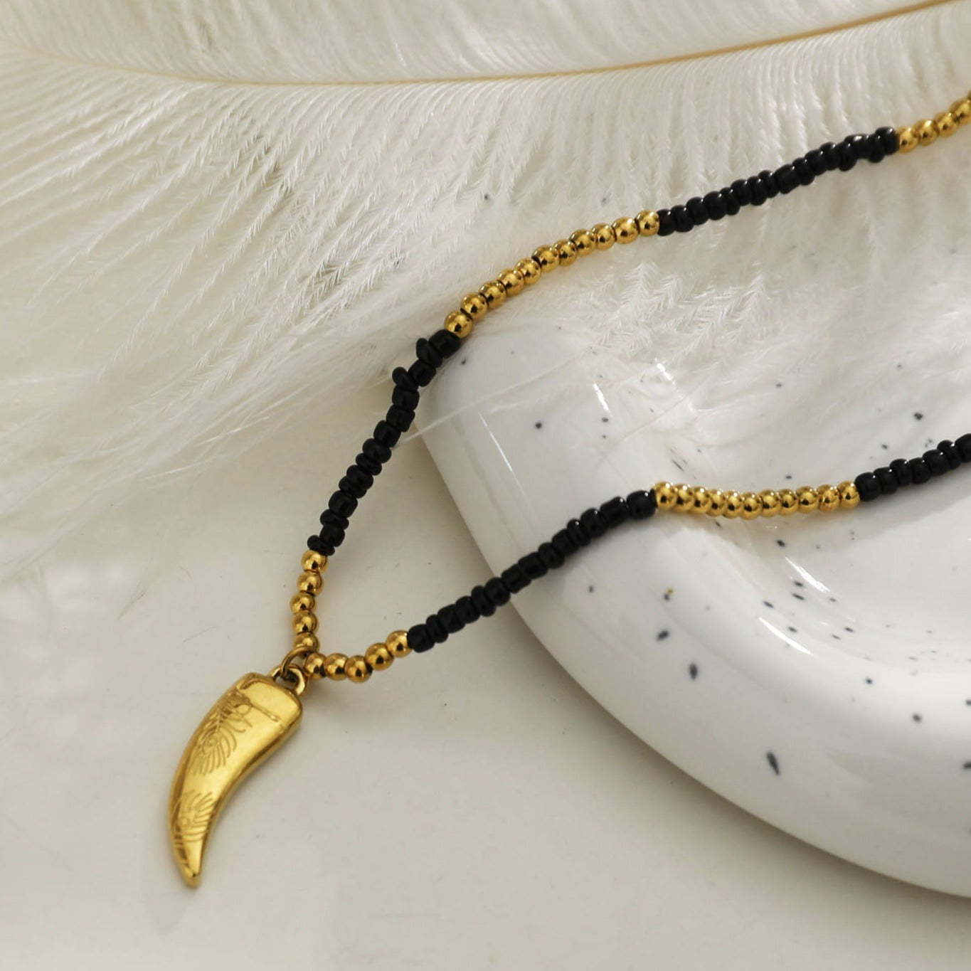 Collier RITA à chaîne perlée noir et or avec pendentif dent en or gravé.