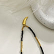 Collier RITA à chaîne perlée noir et or avec pendentif dent en or gravé.