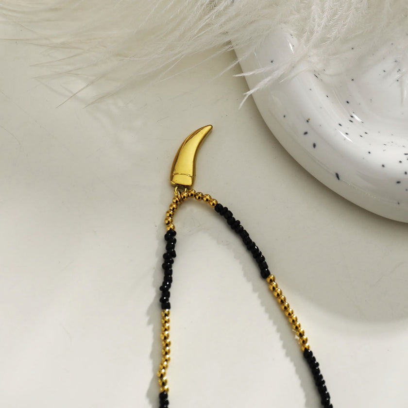 Collier RITA à chaîne perlée noir et or avec pendentif dent en or gravé.