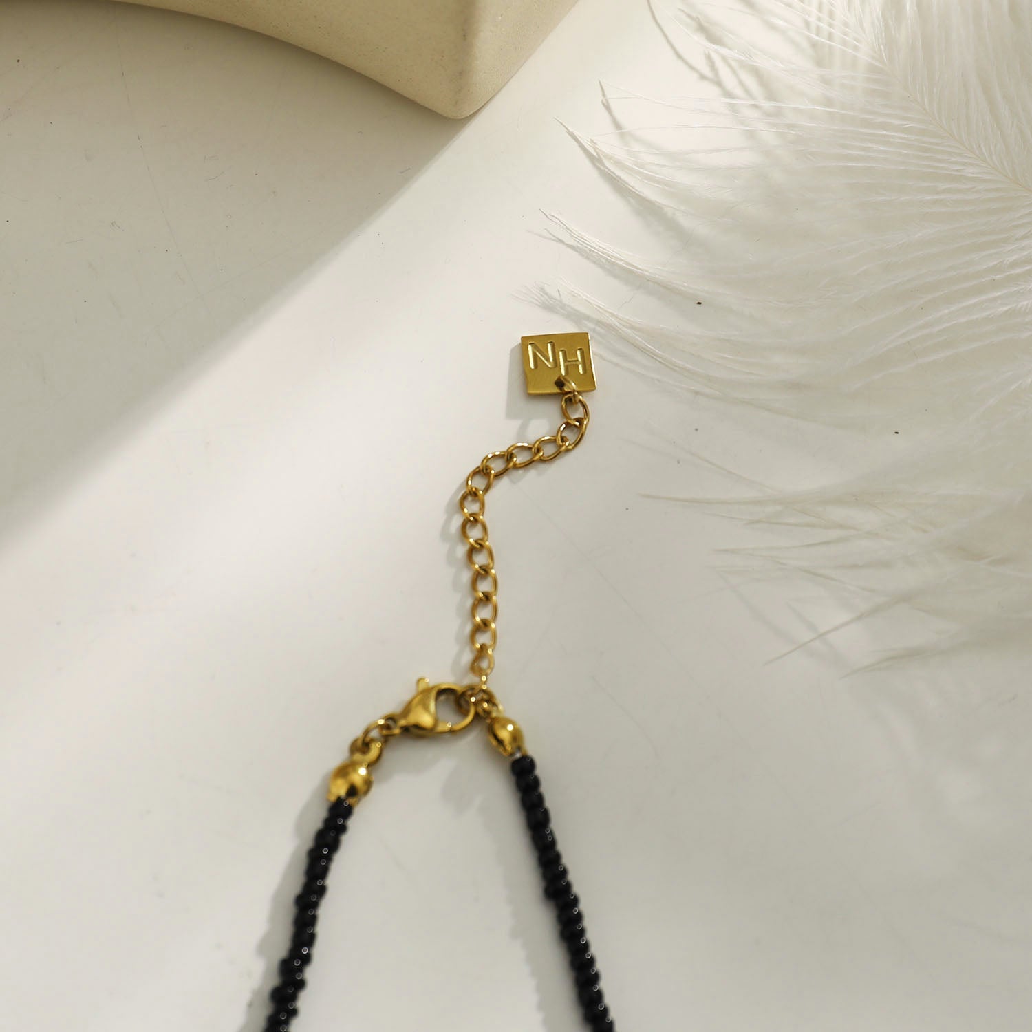 Collier RITA à chaîne perlée noir et or avec pendentif dent en or gravé.