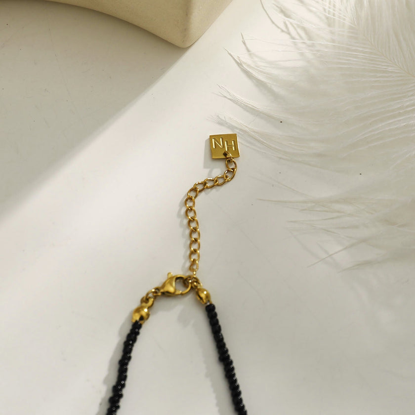 Collier RITA à chaîne perlée noir et or avec pendentif dent en or gravé.